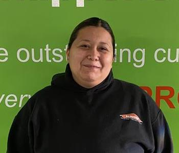 Female employee Imelda Barrera standing in front of a green wall with the SERVPRO logo